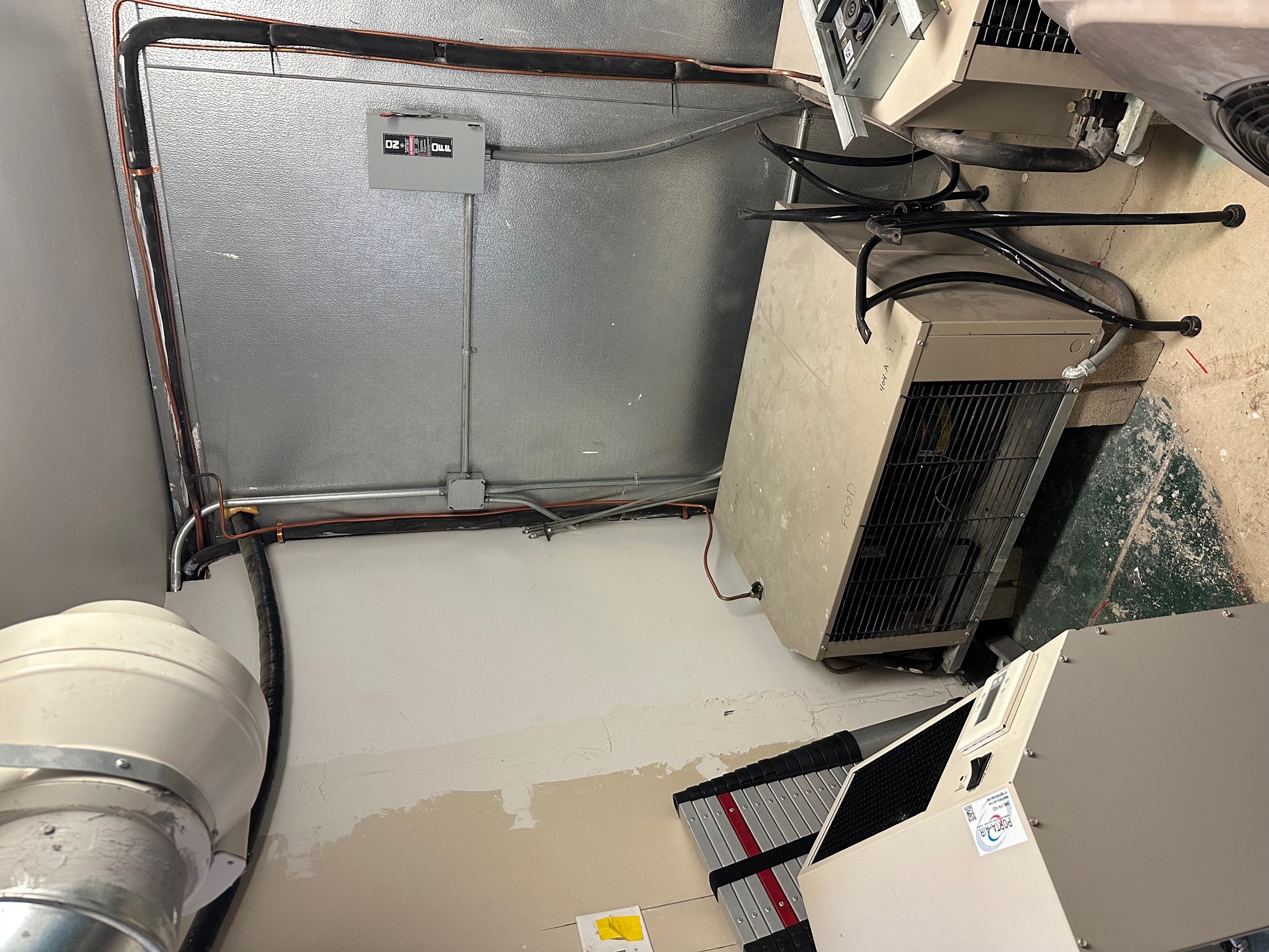 A portable AC unit cooling walk-in refrigerator condensers in the basement of a restaurant. 