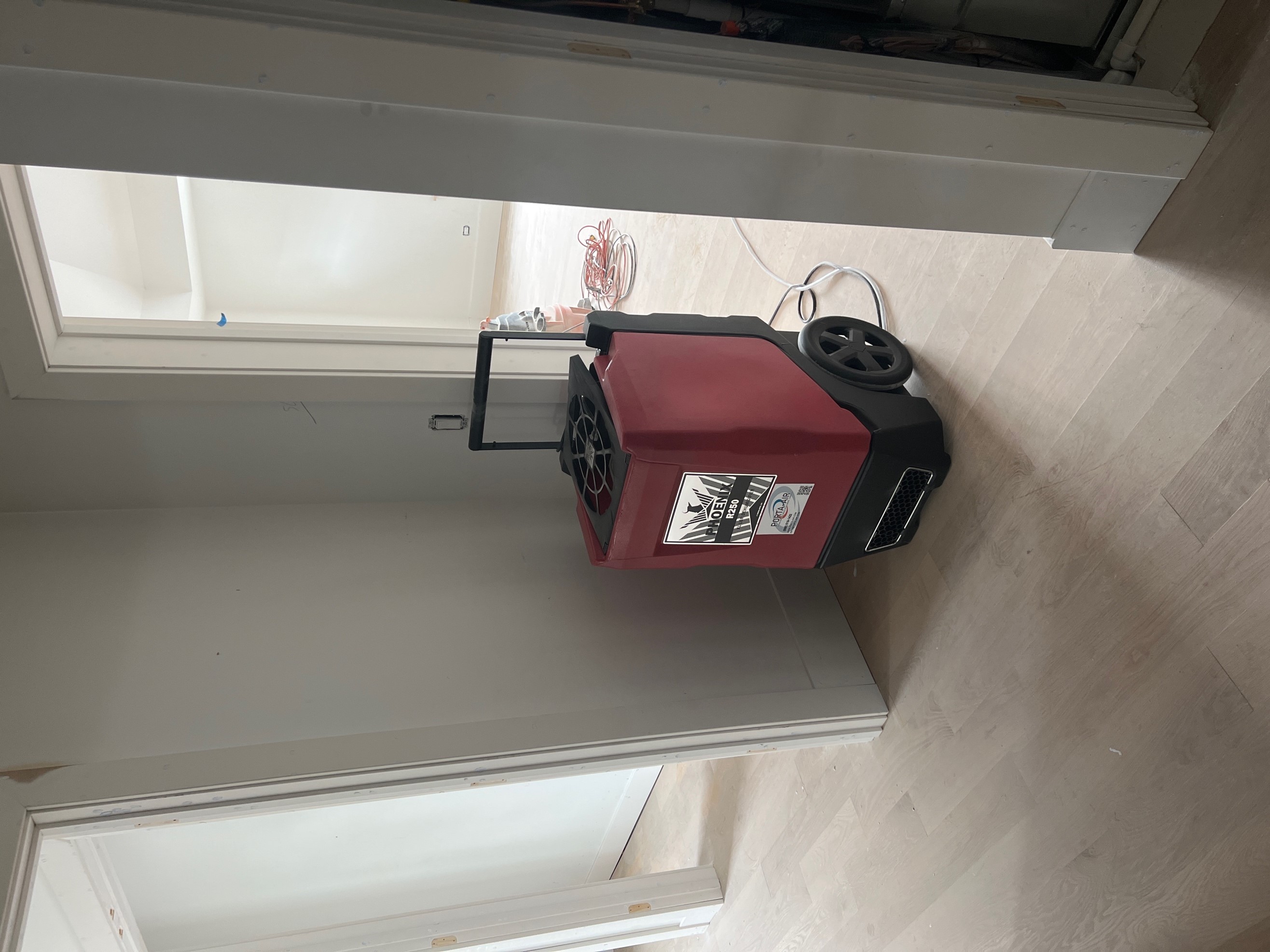 Red portable dehumidifier plugged into the wall outlet inside a new home under construction. 