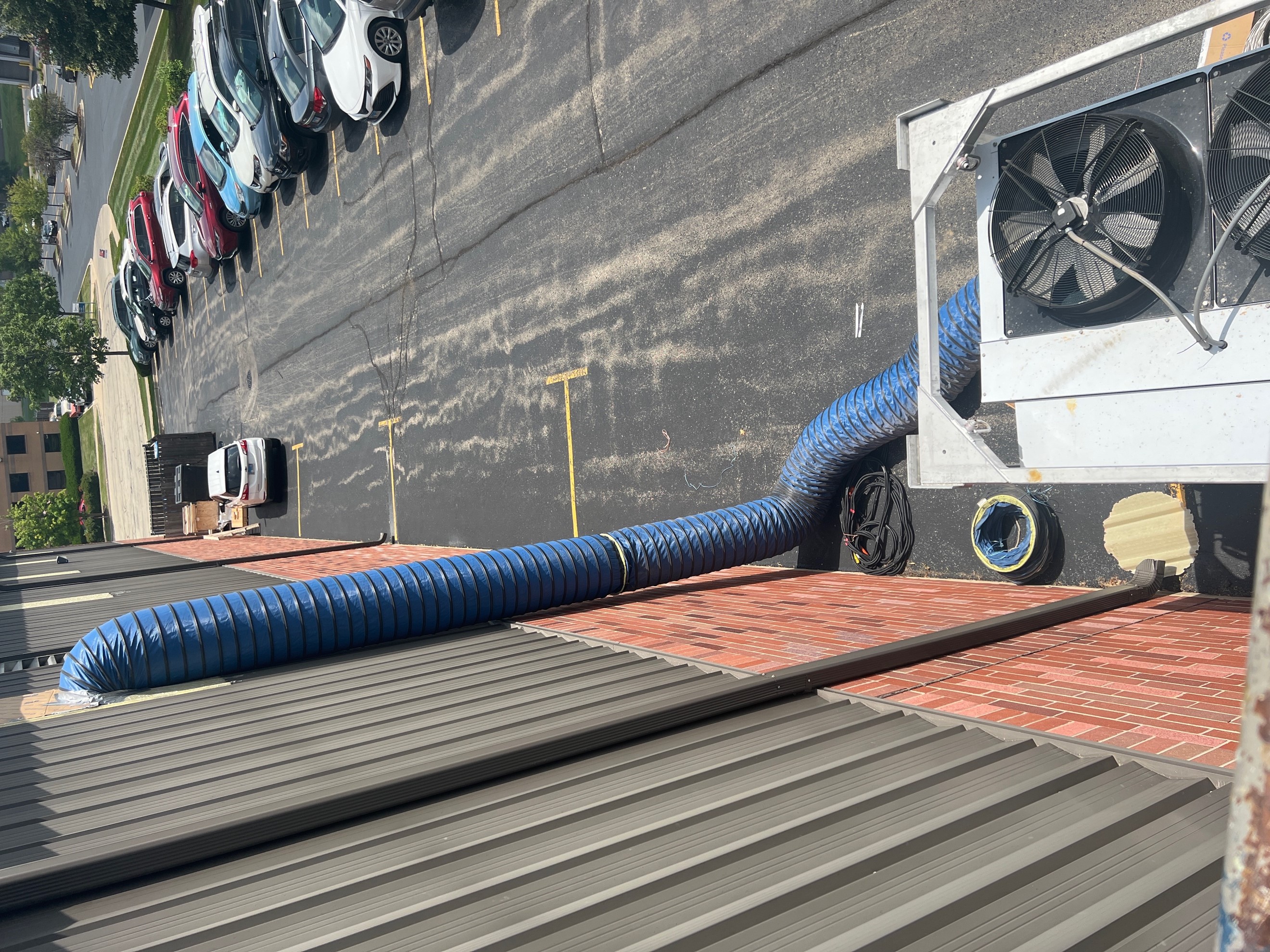 An upper view of a large skid mounted mobile air conditioner showing the return air ductwork going vertically up into a building opening. 