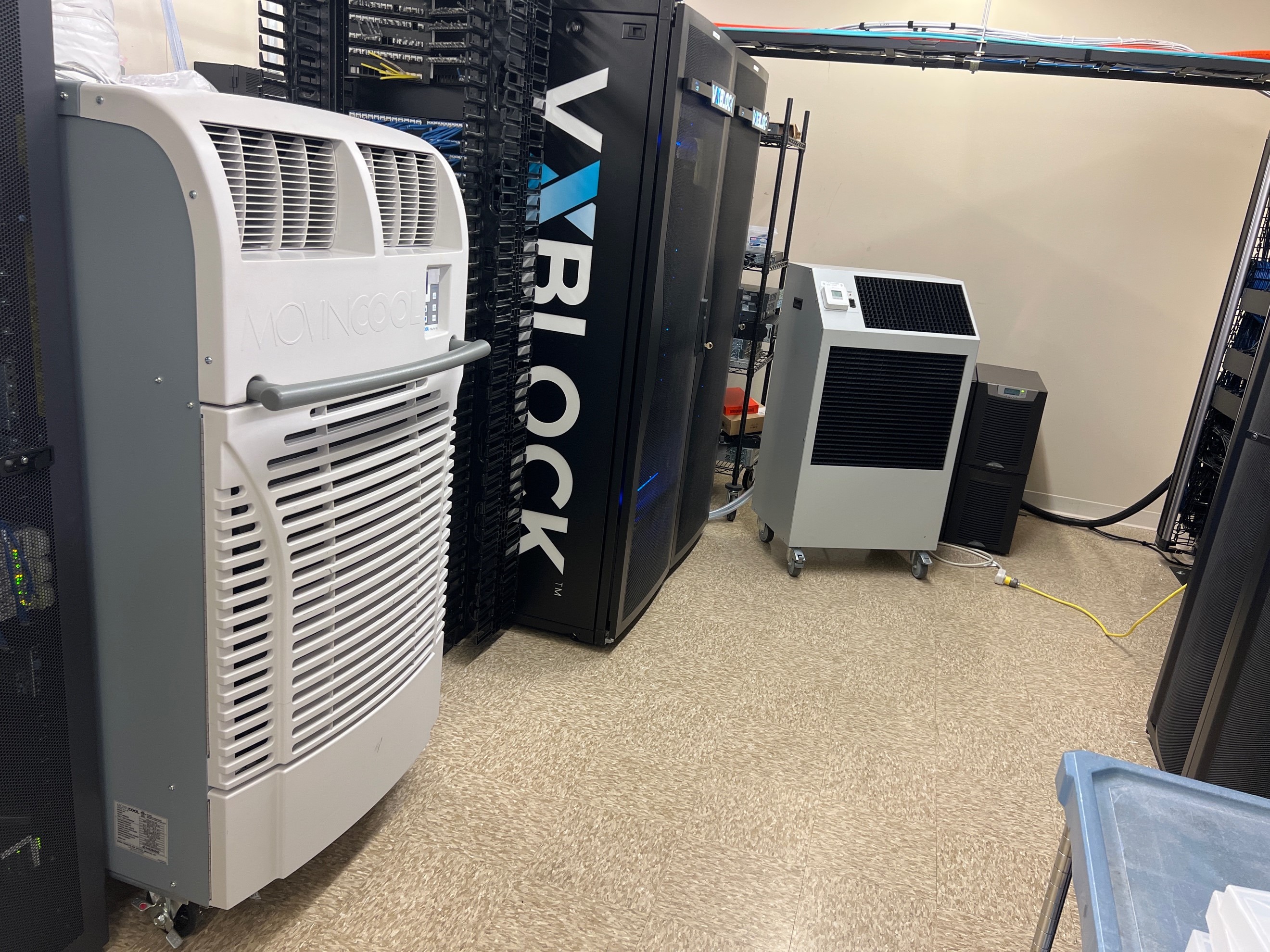 An IT room with two spot cooler rentals on casters cooling the server room hardware. One unit is a Movincool Office Pro 60 air cooled unit; the other unit is a 3-ton water cooled unit.  